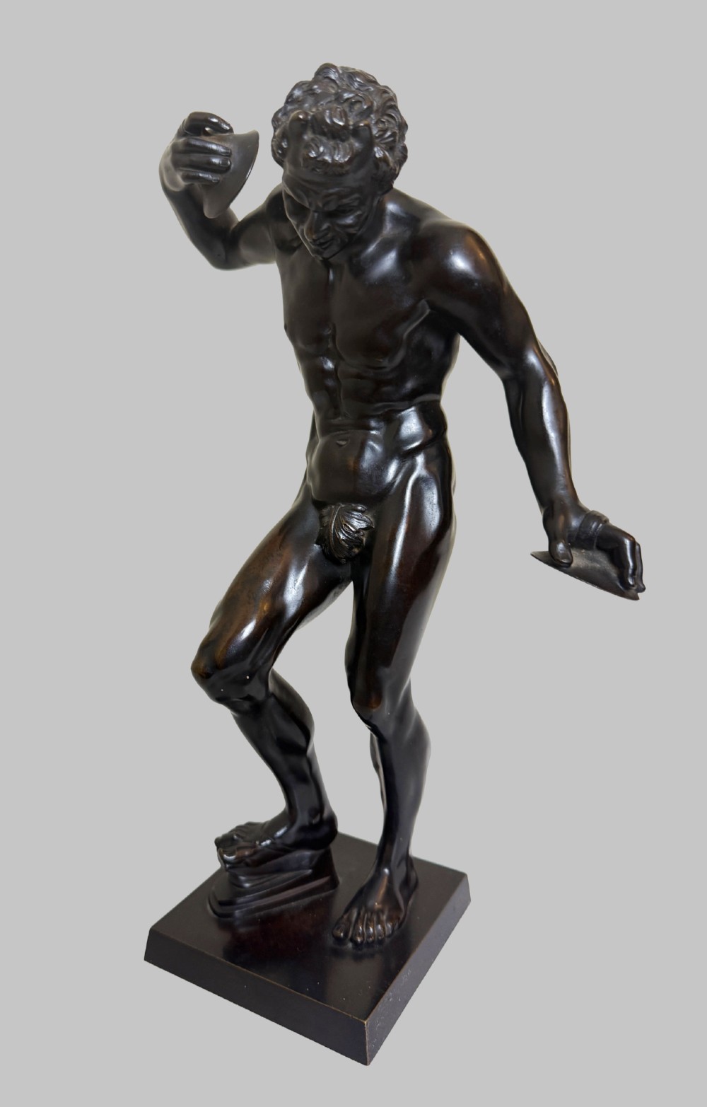 A dark patinated bronze statue depicting a nude classical dancing faun holding cymbals, mounted on a square black base. View V
