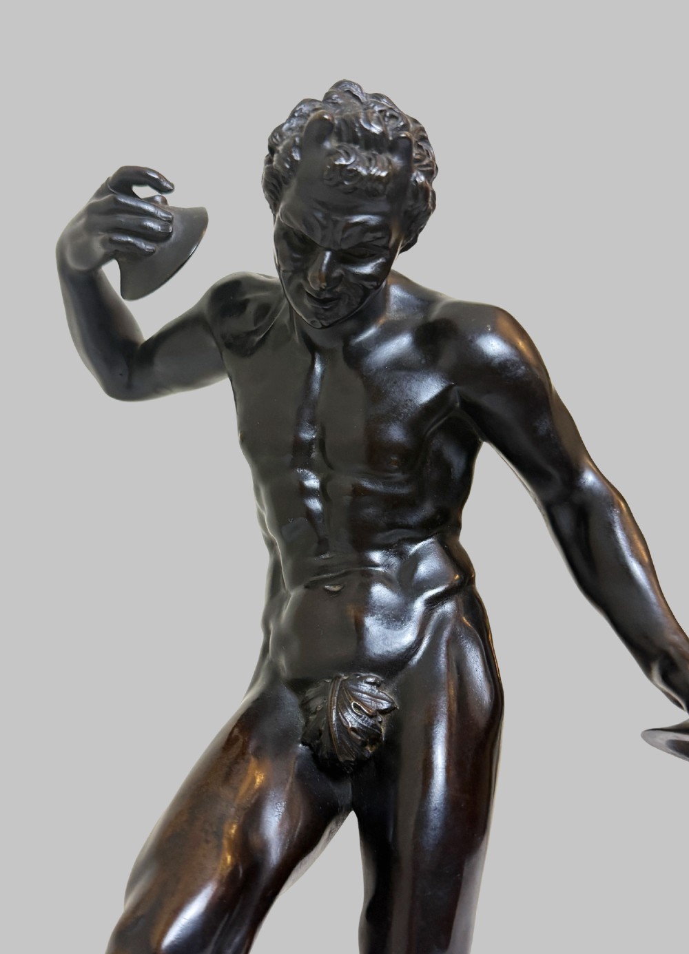 A dark patinated bronze statue depicting a nude classical dancing faun holding cymbals, mounted on a square black base. View VI