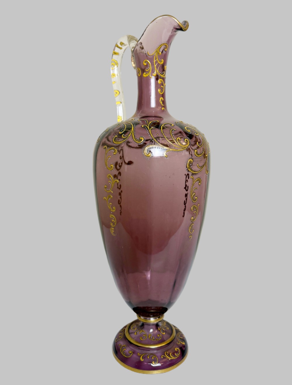 A 19th-century blown violet glass ewer featuring a clear glass handle, slender neck, circular base, and hand-painted gilt scroll patterns. View II
