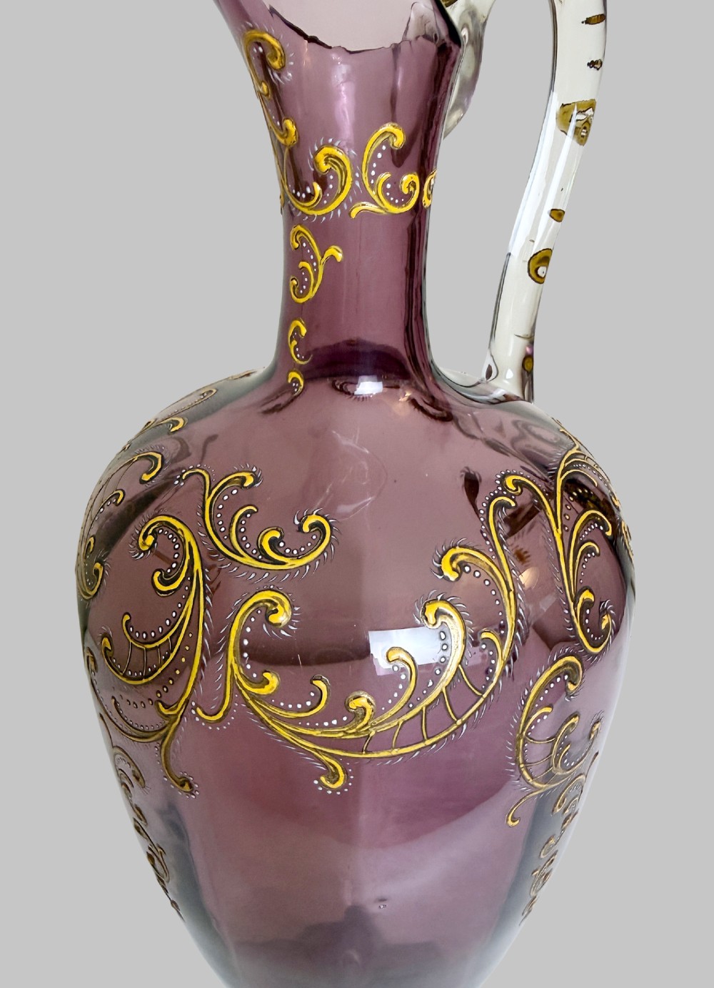 A 19th-century blown violet glass ewer featuring a clear glass handle, slender neck, circular base, and hand-painted gilt scroll patterns. View III
