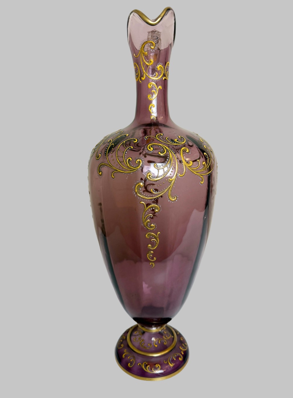 A 19th-century blown violet glass ewer featuring a clear glass handle, slender neck, circular base, and hand-painted gilt scroll patterns. View V