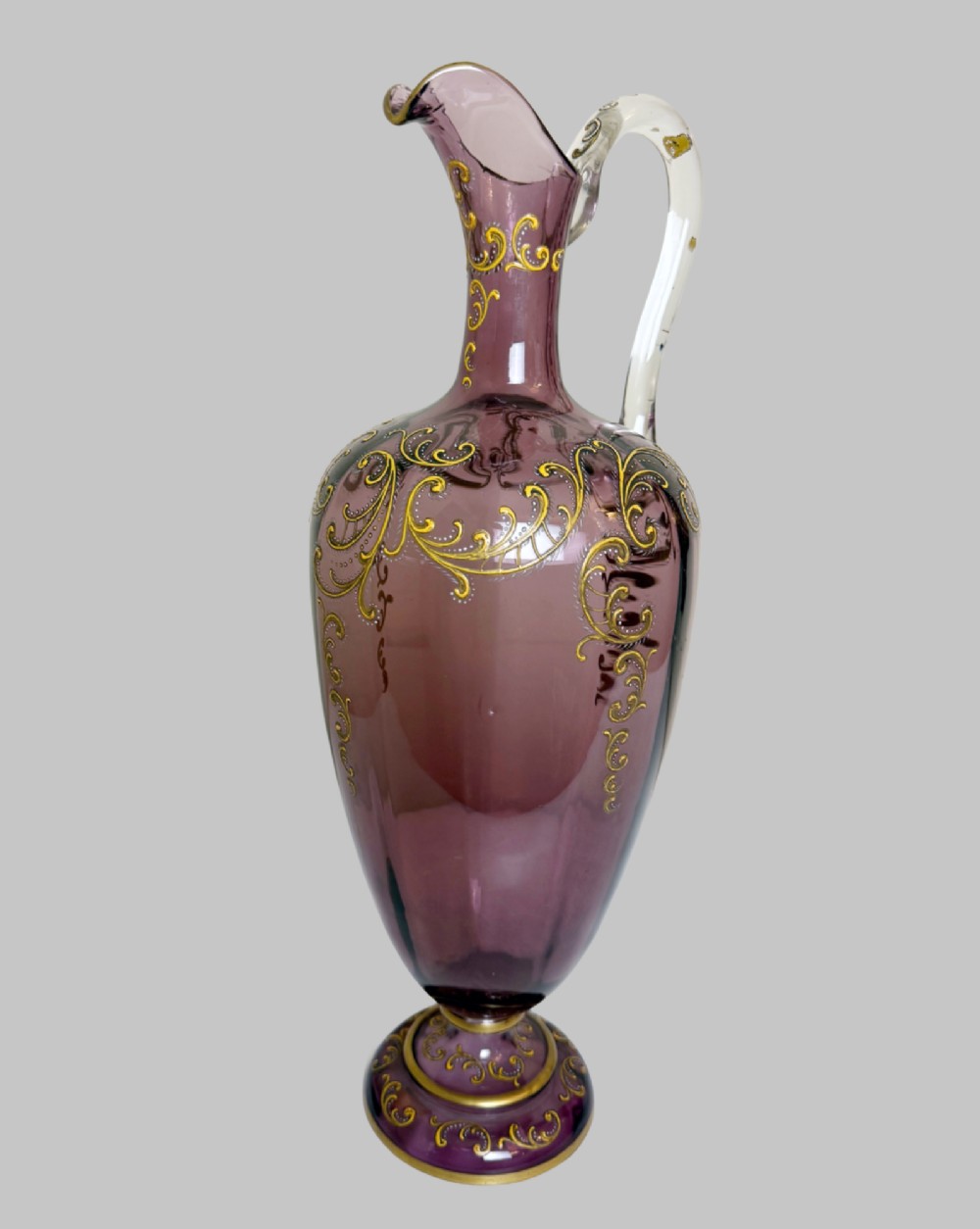 A 19th-century blown violet glass ewer featuring a clear glass handle, slender neck, circular base, and hand-painted gilt scroll patterns. View VIII