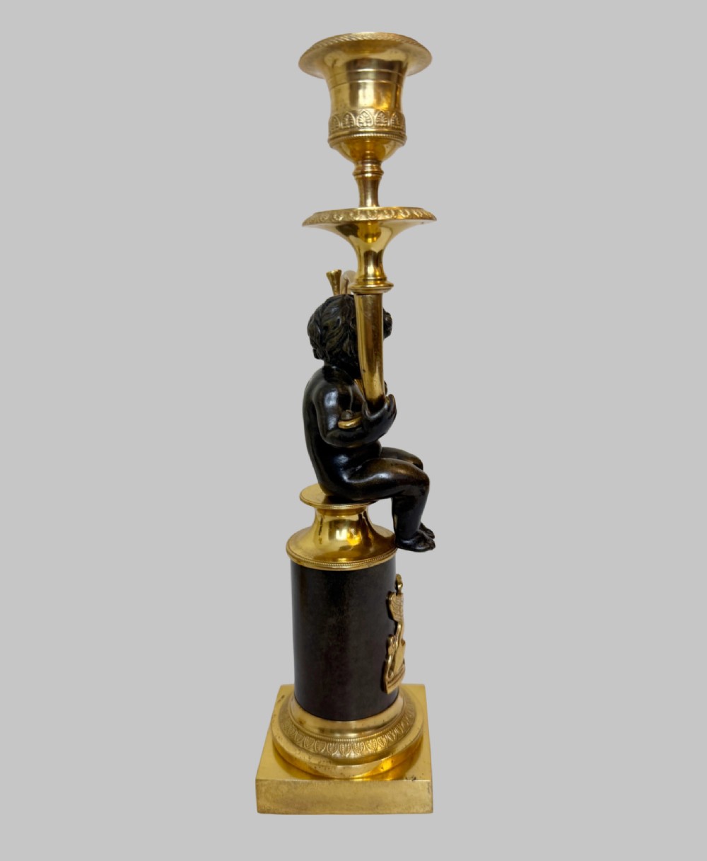 A pair of 19th-century gilt and patinated bronze candlesticks featuring dark cherubs seated on cylindrical pedestals with gilt winged lion motifs, holding gold-toned horn sconces. View III