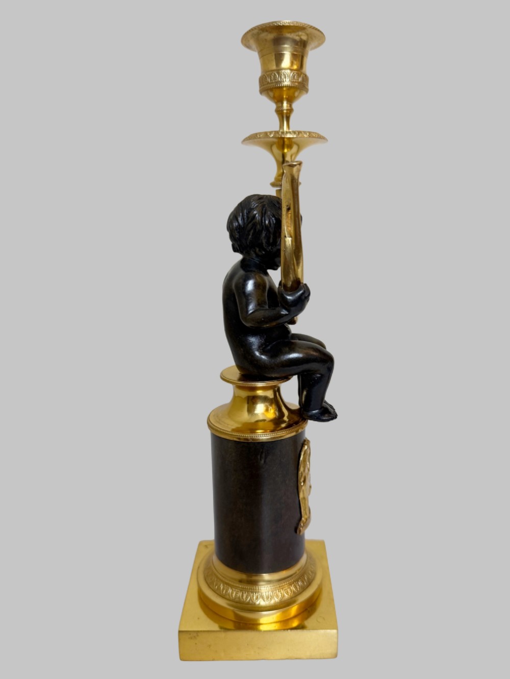 A pair of 19th-century gilt and patinated bronze candlesticks featuring dark cherubs seated on cylindrical pedestals with gilt winged lion motifs, holding gold-toned horn sconces. View IV