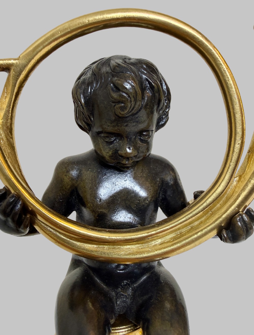 A pair of 19th-century gilt and patinated bronze candlesticks featuring dark cherubs seated on cylindrical pedestals with gilt winged lion motifs, holding gold-toned horn sconces. View V