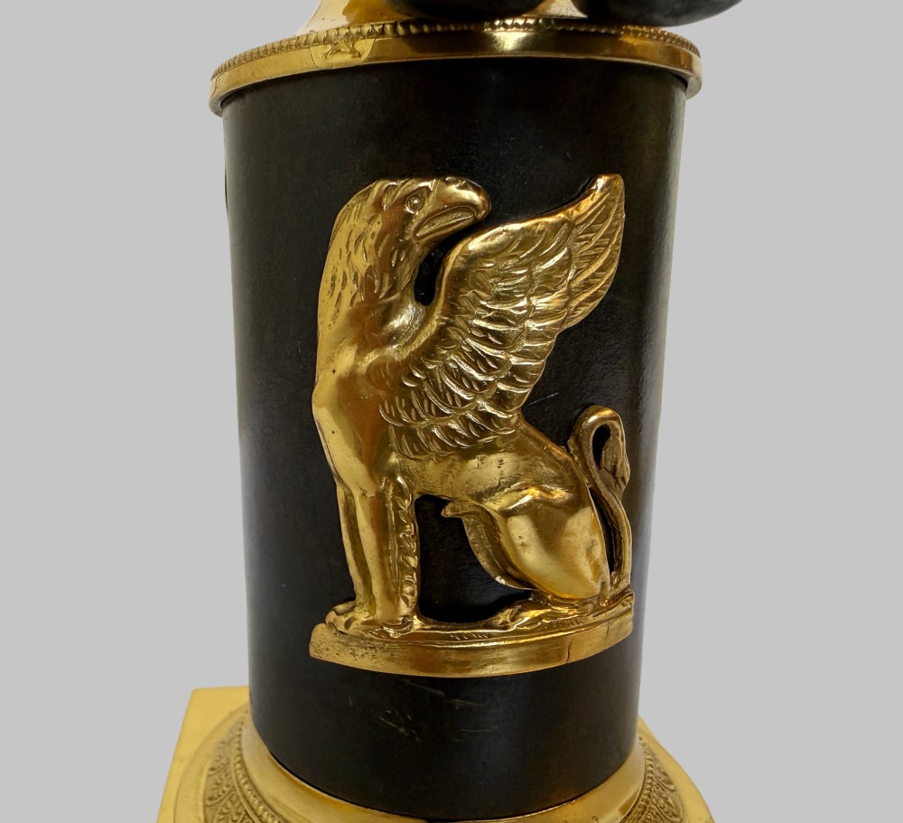 A pair of 19th-century gilt and patinated bronze candlesticks featuring dark cherubs seated on cylindrical pedestals with gilt winged lion motifs, holding gold-toned horn sconces. View VIII
