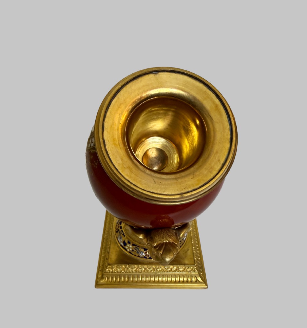 A 19th-century porcelain vase featuring hand-painted cherubs, deep red ground panels, gilded filigree, and a square gilt-bronze foot with enamel accents. View III