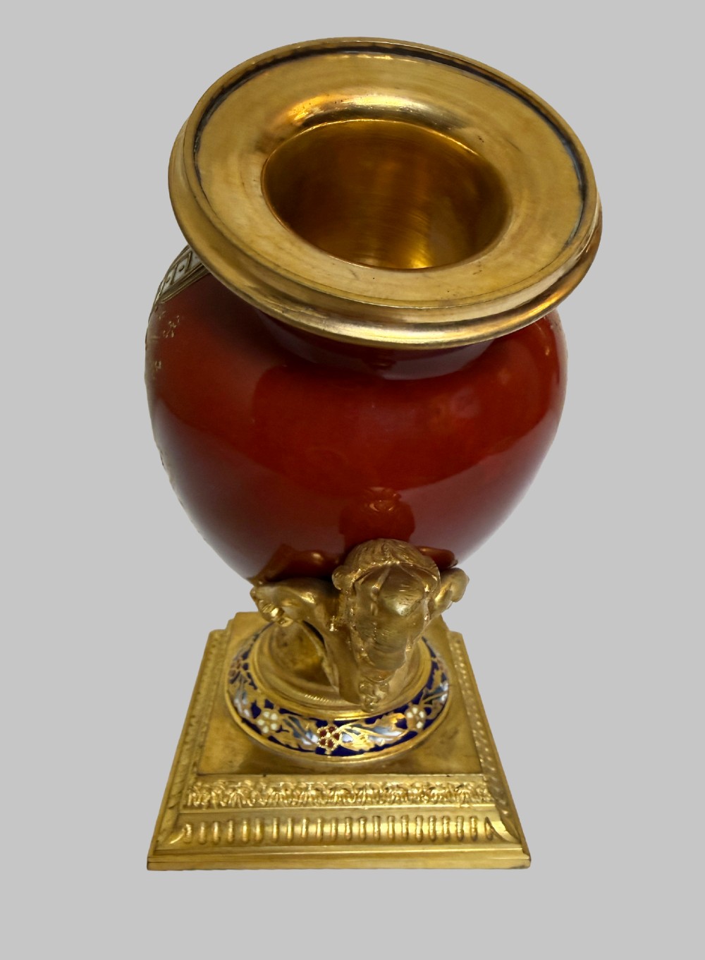 A 19th-century porcelain vase featuring hand-painted cherubs, deep red ground panels, gilded filigree, and a square gilt-bronze foot with enamel accents. View IV