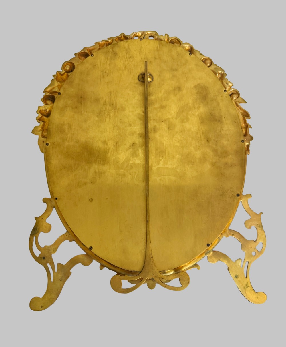 An antique oval gilt bronze picture frame featuring relief floral garlands, scrollwork legs, and a blue moire silk mount. View IV