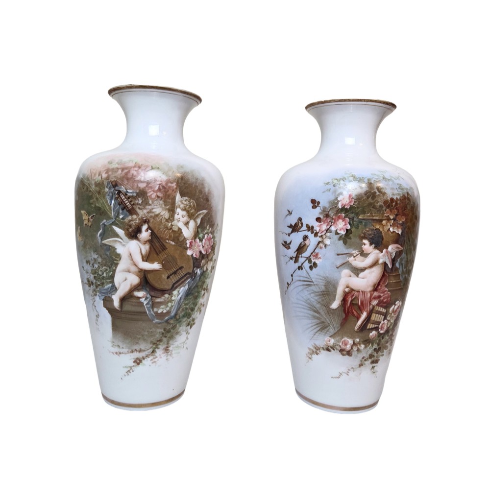A pair of white porcelain baluster vases decorated with painted scenes of cherubs playing musical instruments in a garden, finished with gilt rims.