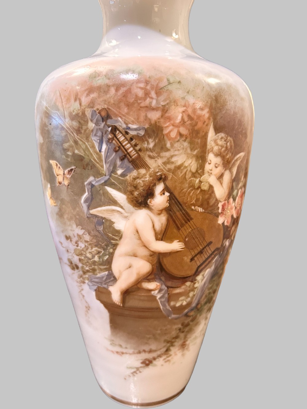 A pair of white porcelain baluster vases decorated with painted scenes of cherubs playing musical instruments in a garden, finished with gilt rims. View II