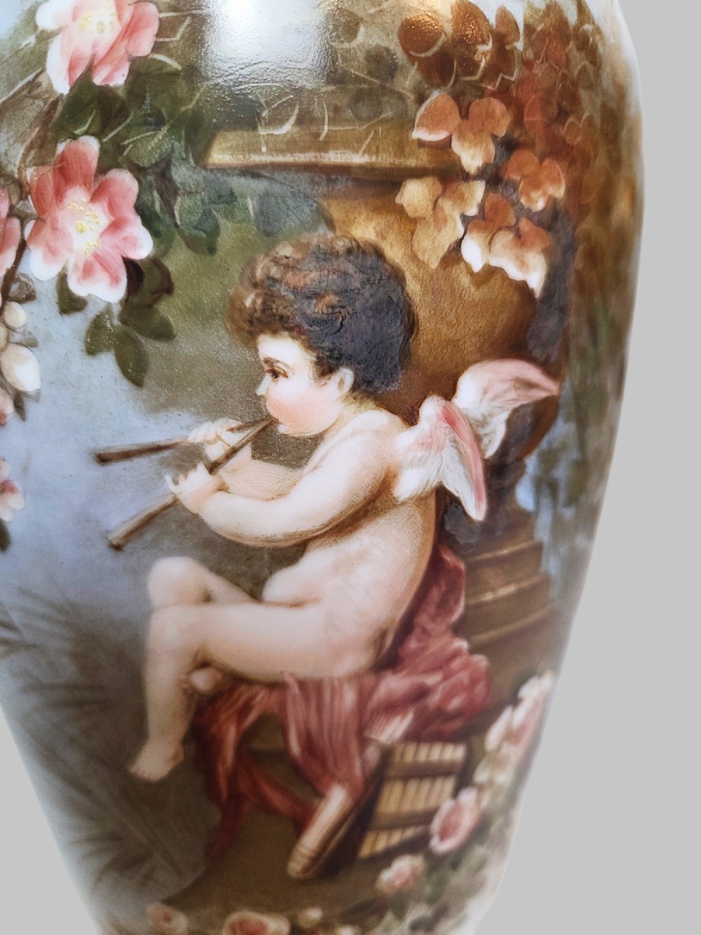 A pair of white porcelain baluster vases decorated with painted scenes of cherubs playing musical instruments in a garden, finished with gilt rims. View IV