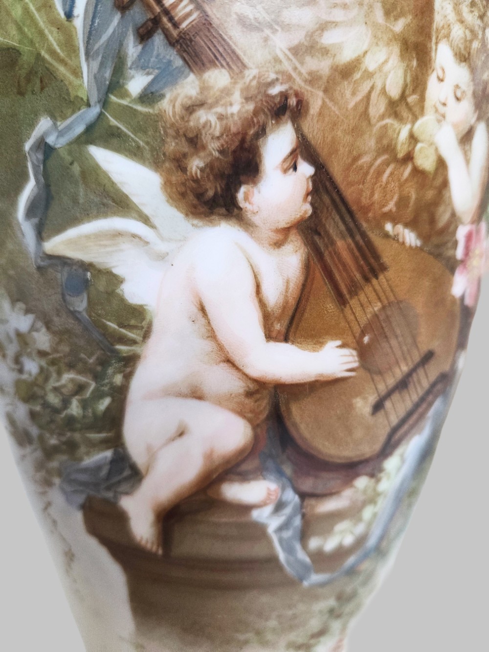 A pair of white porcelain baluster vases decorated with painted scenes of cherubs playing musical instruments in a garden, finished with gilt rims. View V