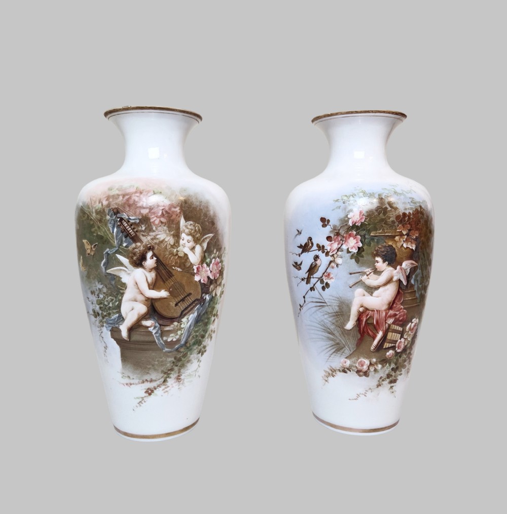 A pair of white porcelain baluster vases decorated with painted scenes of cherubs playing musical instruments in a garden, finished with gilt rims. View VII