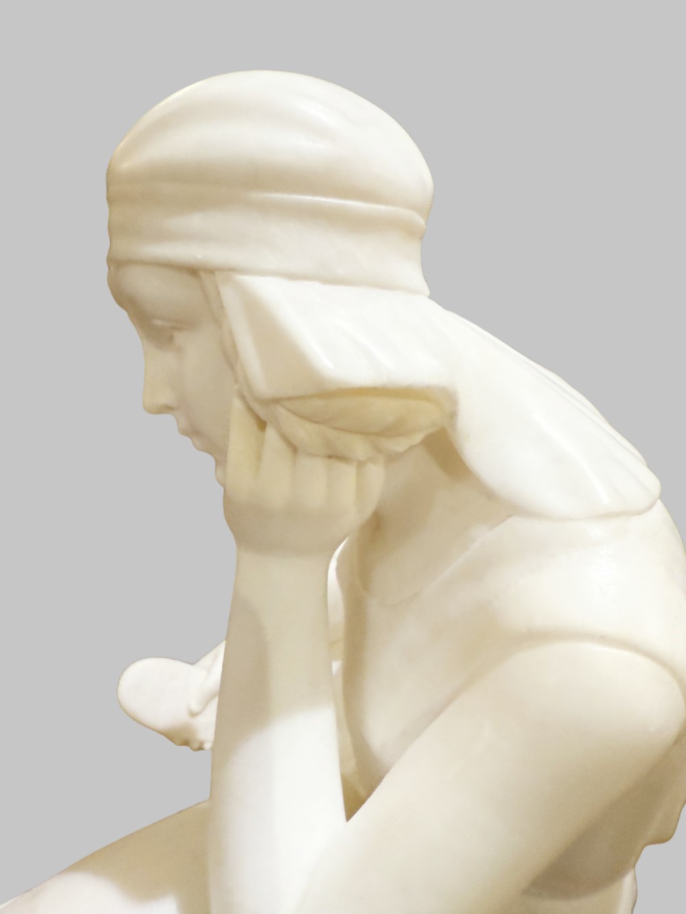A carved white alabaster sculpture depicting a seated young maiden resting her chin on her hand beside a pitcher, mounted on a rectangular honey-coloured marble base. View II