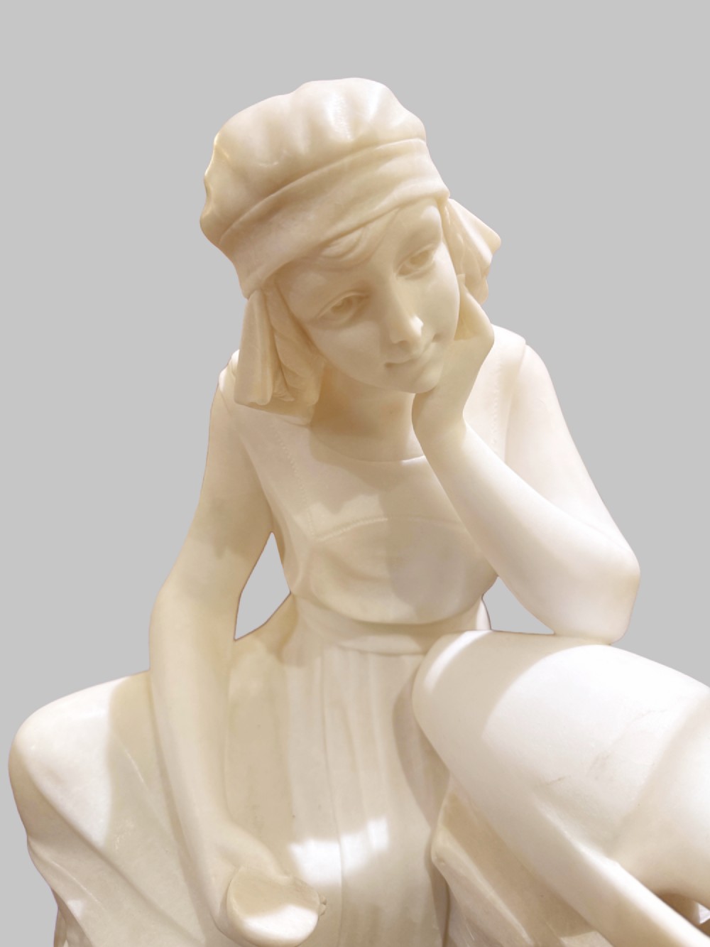 A carved white alabaster sculpture depicting a seated young maiden resting her chin on her hand beside a pitcher, mounted on a rectangular honey-coloured marble base. View IV