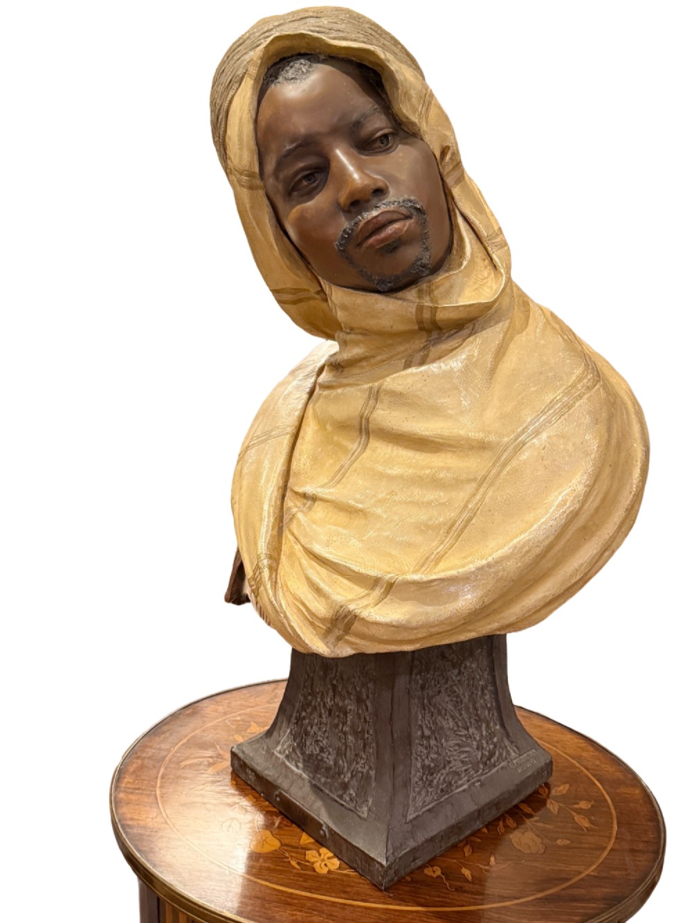 A cold-painted polychrome terracotta bust of a young North African man wearing a draped yellow headscarf mounted on a dark pedestal base.