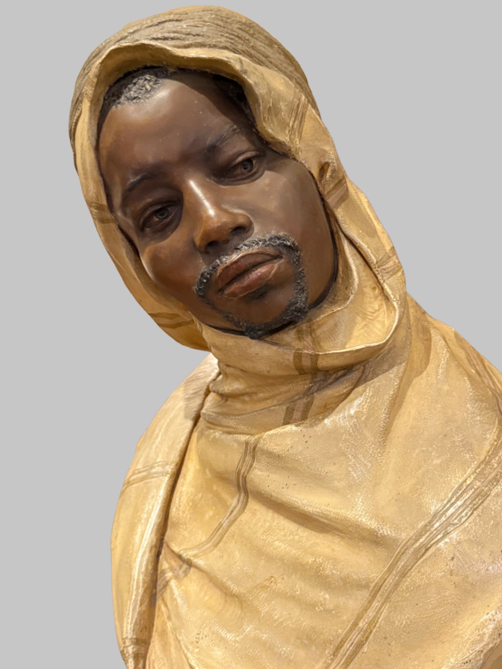 A cold-painted polychrome terracotta bust of a young North African man wearing a draped yellow headscarf mounted on a dark pedestal base. View II
