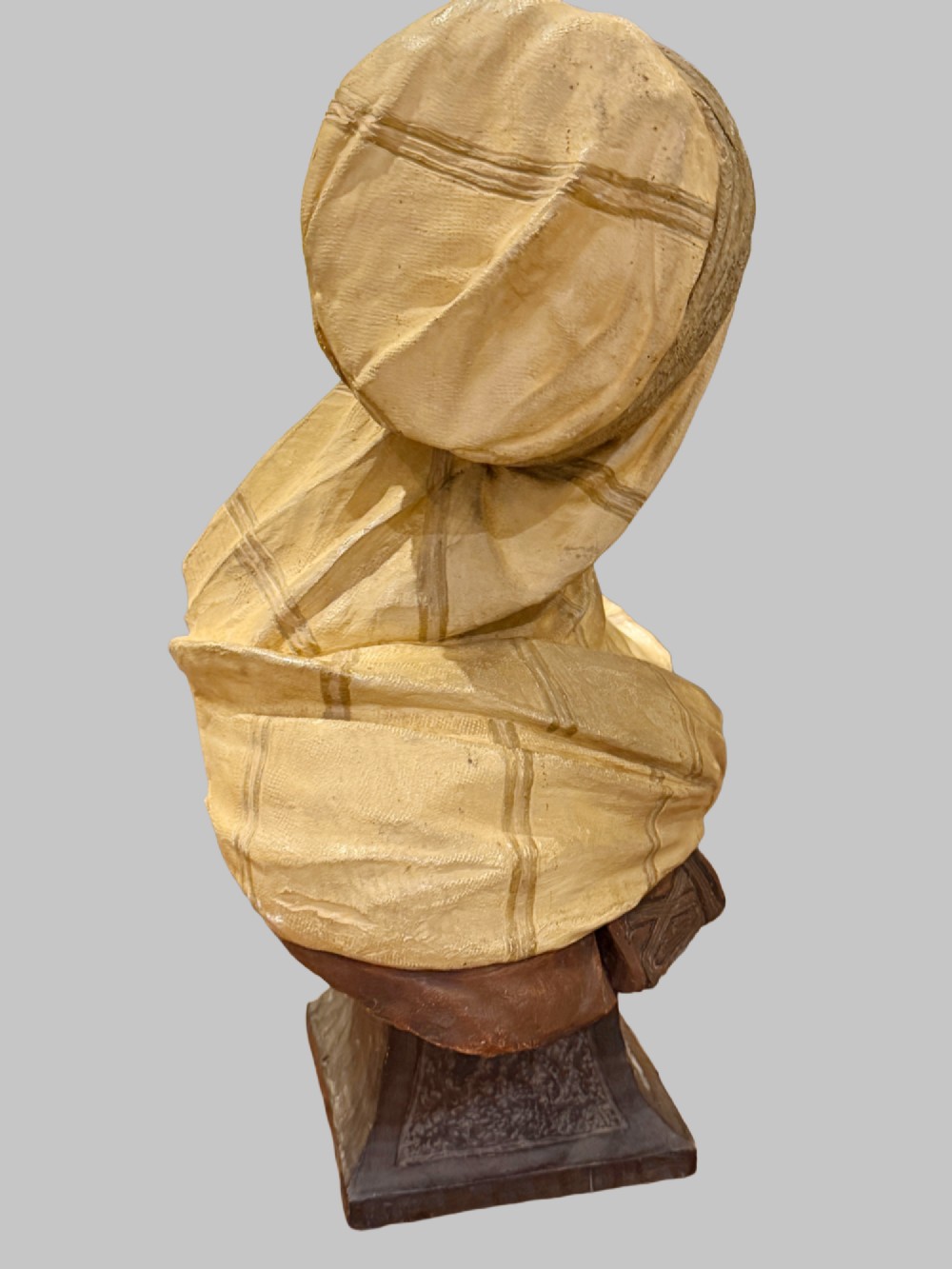 A cold-painted polychrome terracotta bust of a young North African man wearing a draped yellow headscarf mounted on a dark pedestal base. View V