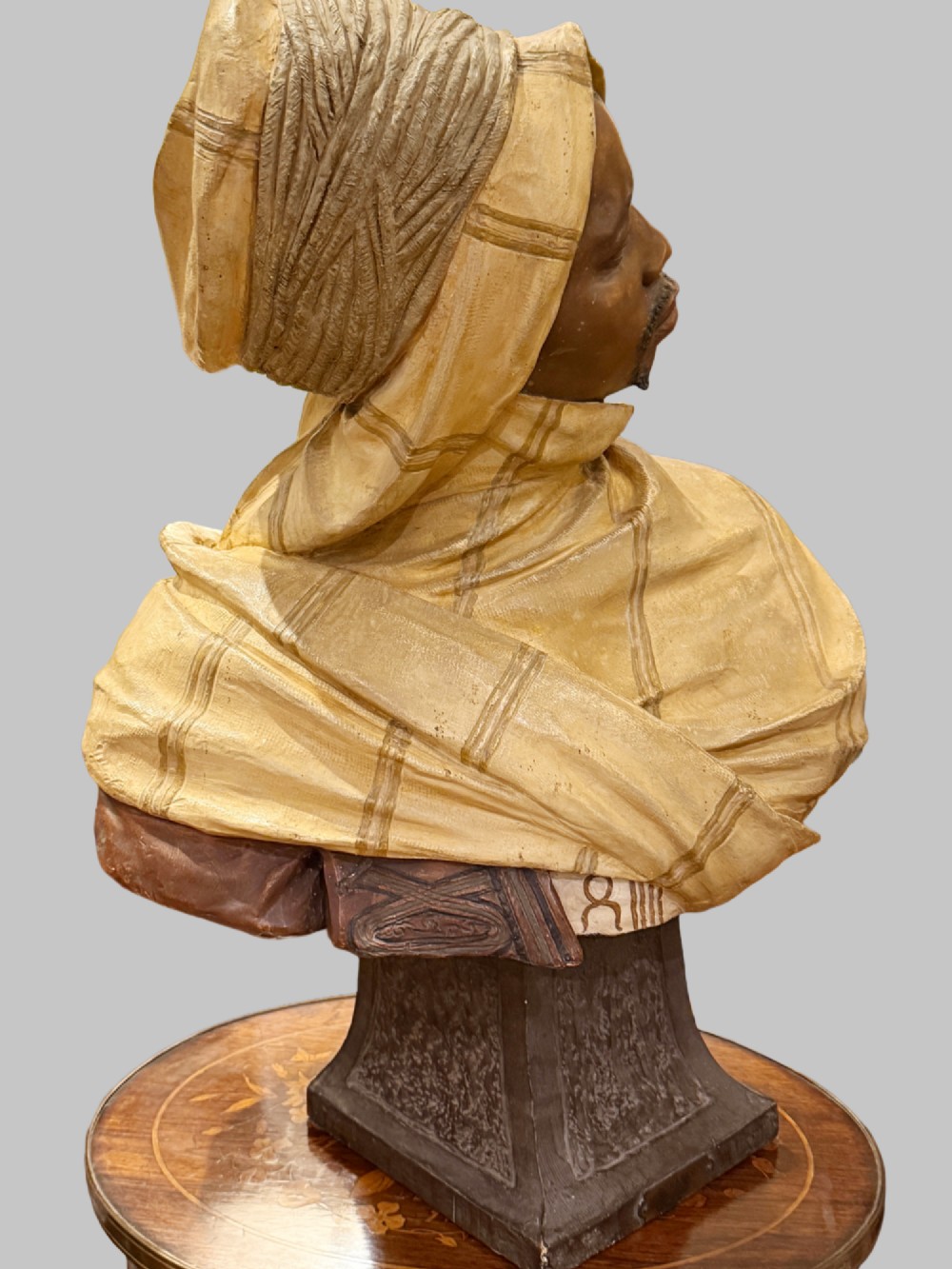 A cold-painted polychrome terracotta bust of a young North African man wearing a draped yellow headscarf mounted on a dark pedestal base. View VI