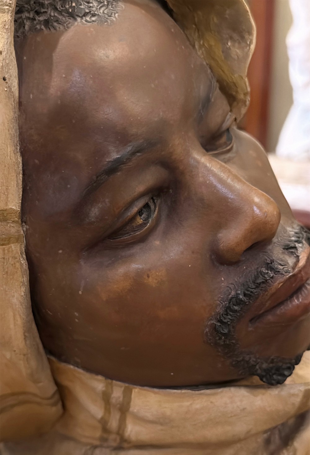 A cold-painted polychrome terracotta bust of a young North African man wearing a draped yellow headscarf mounted on a dark pedestal base. View VII