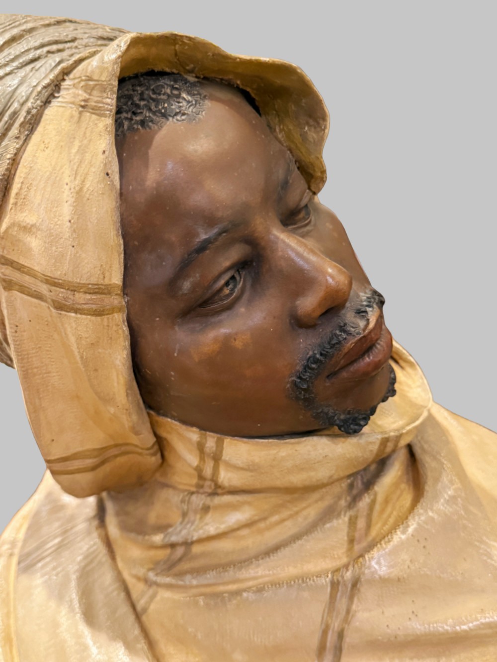 A cold-painted polychrome terracotta bust of a young North African man wearing a draped yellow headscarf mounted on a dark pedestal base. View VIII
