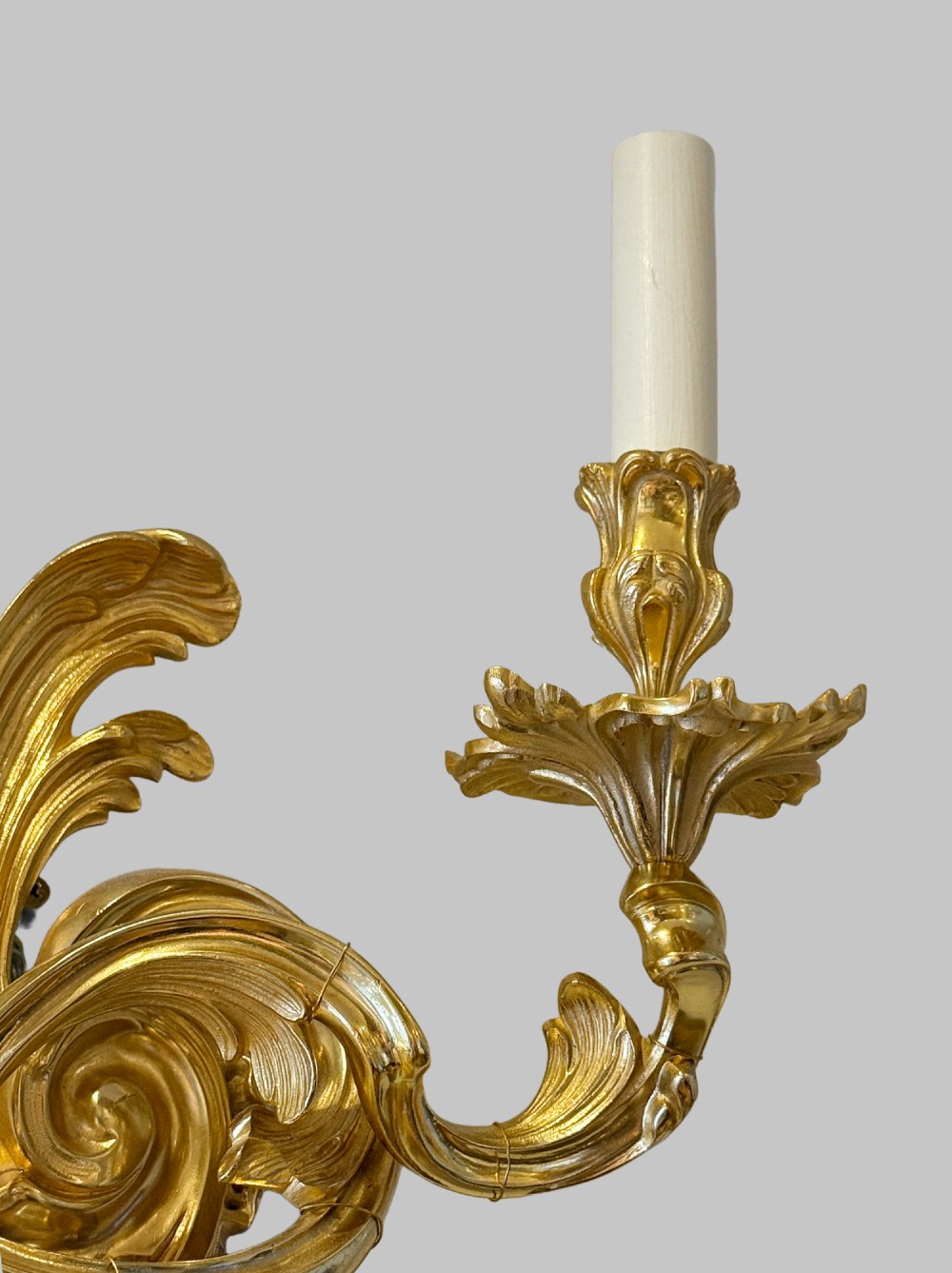 A pair of gilt bronze two-light wall sconces featuring elaborate Rococo scrolling acanthus leaf metalwork and cream candle sleeves. View III