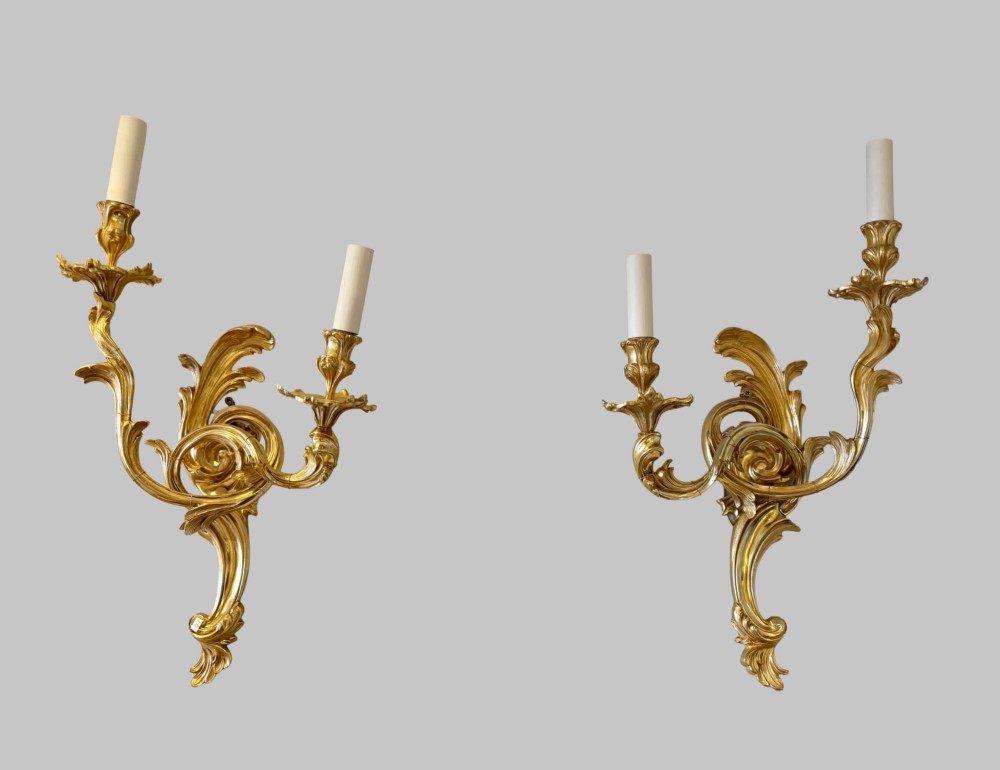 A pair of gilt bronze two-light wall sconces featuring elaborate Rococo scrolling acanthus leaf metalwork and cream candle sleeves. View VIII