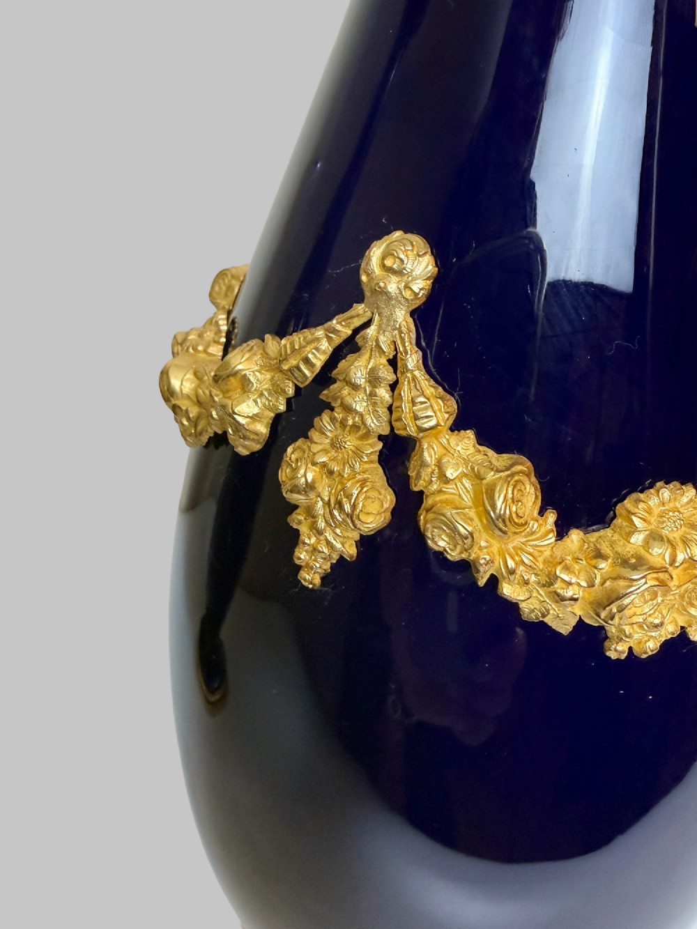 A pair of 19th-century deep cobalt blue porcelain vases decorated with gilt bronze floral garland swags and gilded rim bases. View V