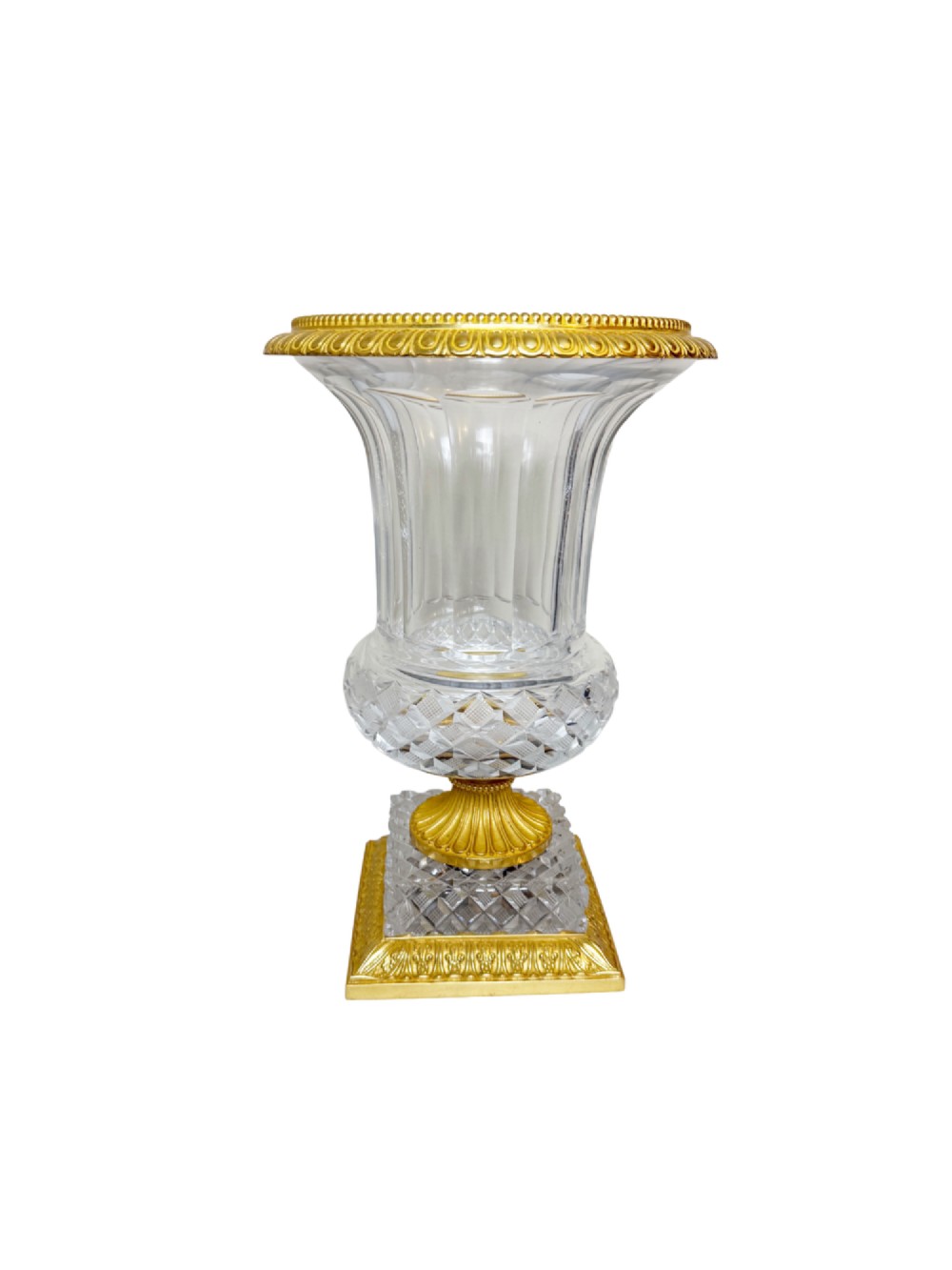 A clear cut-crystal urn-shaped vase featuring fluted body detailing, diamond-pattern cutting, and a gilt bronze rim and square pedestal base.