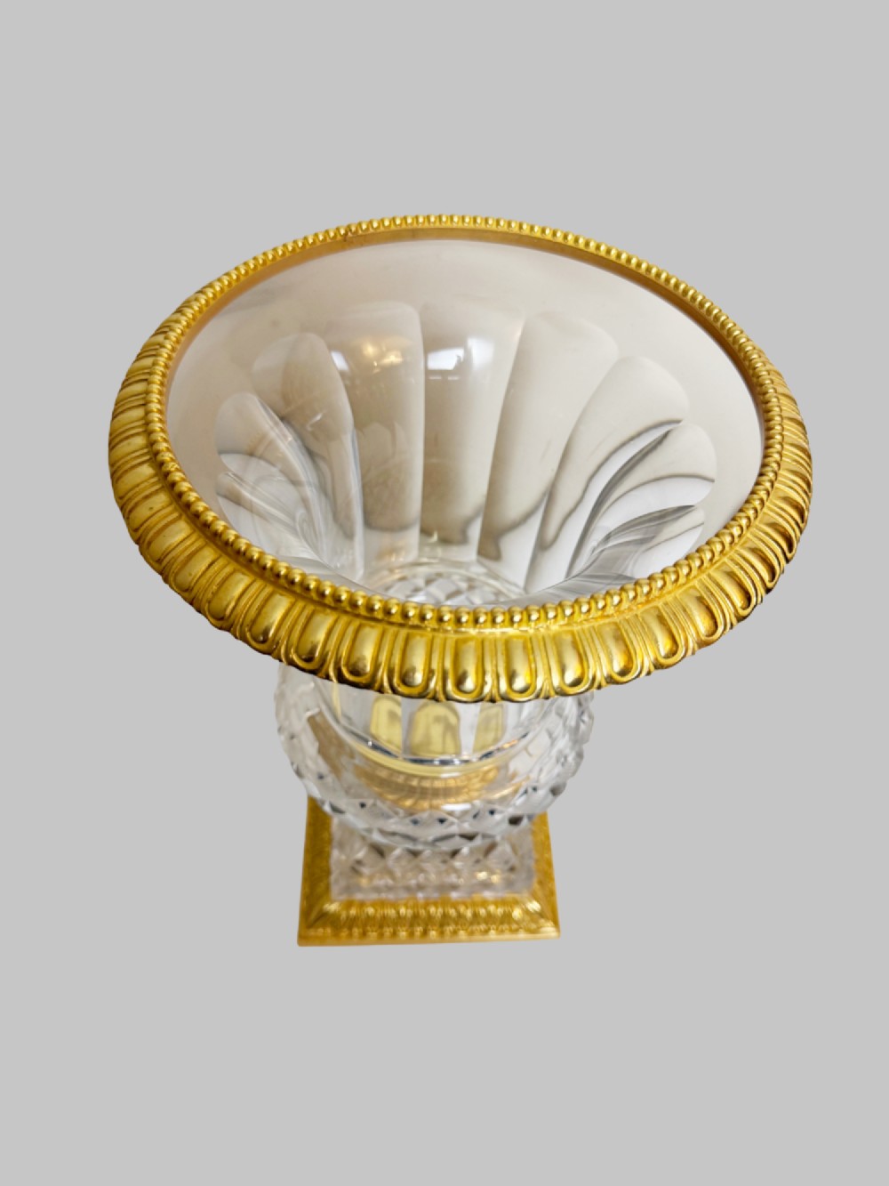 A clear cut-crystal urn-shaped vase featuring fluted body detailing, diamond-pattern cutting, and a gilt bronze rim and square pedestal base. View V
