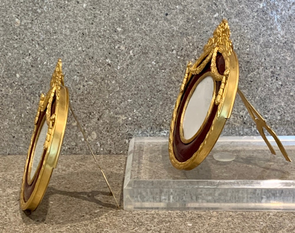 A pair of circular French Napoleon III gilt bronze and red enamel picture frames featuring decorative bow crests and floral garland detailing. View IV