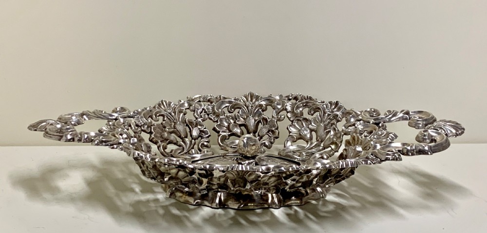 An oval antique silver basket featuring intricate openwork scrollwork, foliage motifs, and two integrated side handles. View V