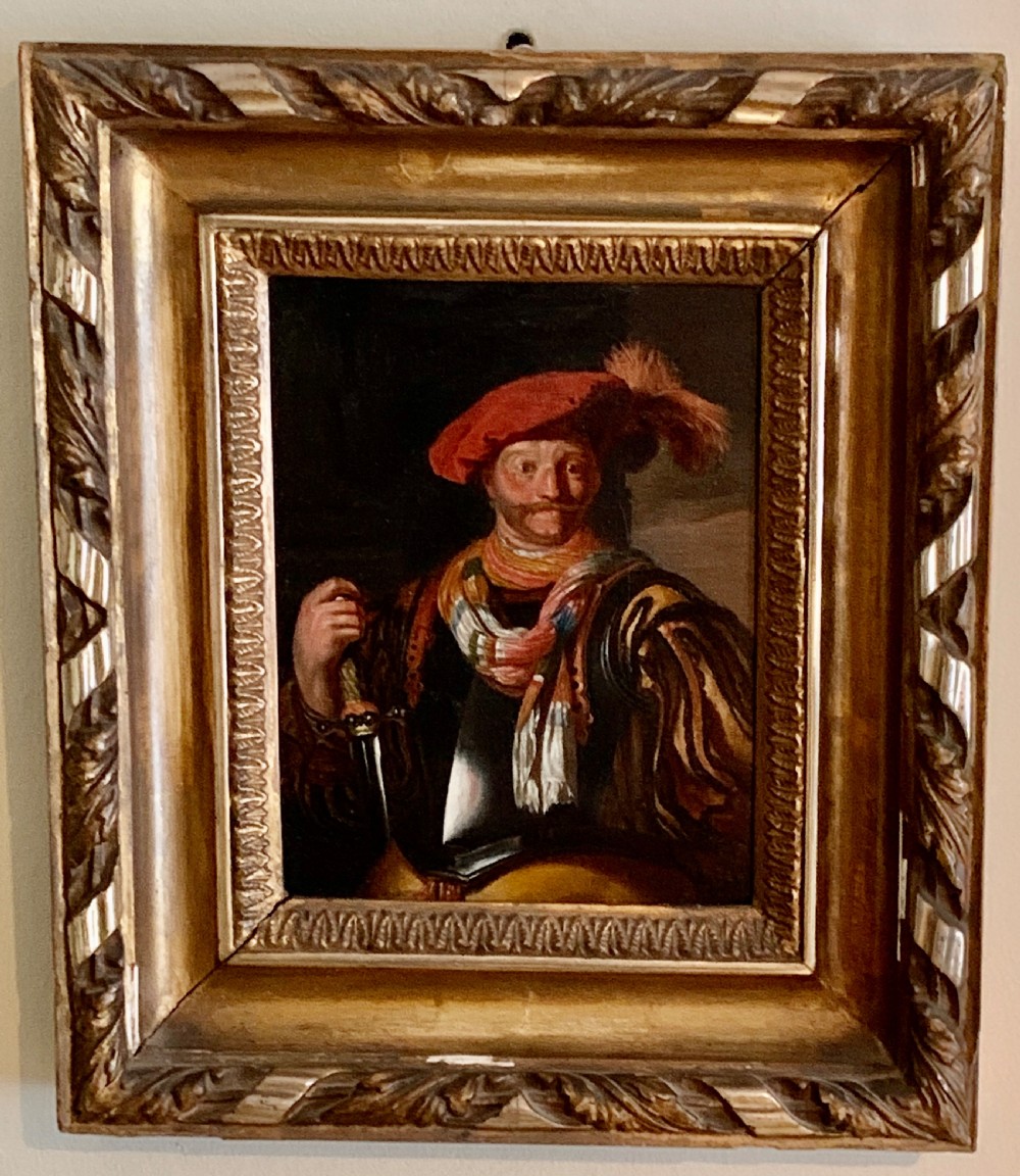 A framed half-length oil painting depicting a cavalier figure wearing a red feathered hat and a striped scarf while holding a sword hilt.