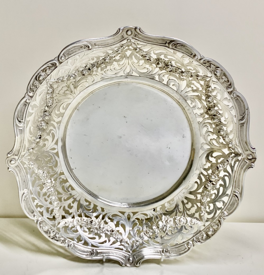 A circular antique solid silver bread basket featuring intricate hand-pierced fretwork, repousse floral swags, and a contoured scalloped rim. View II
