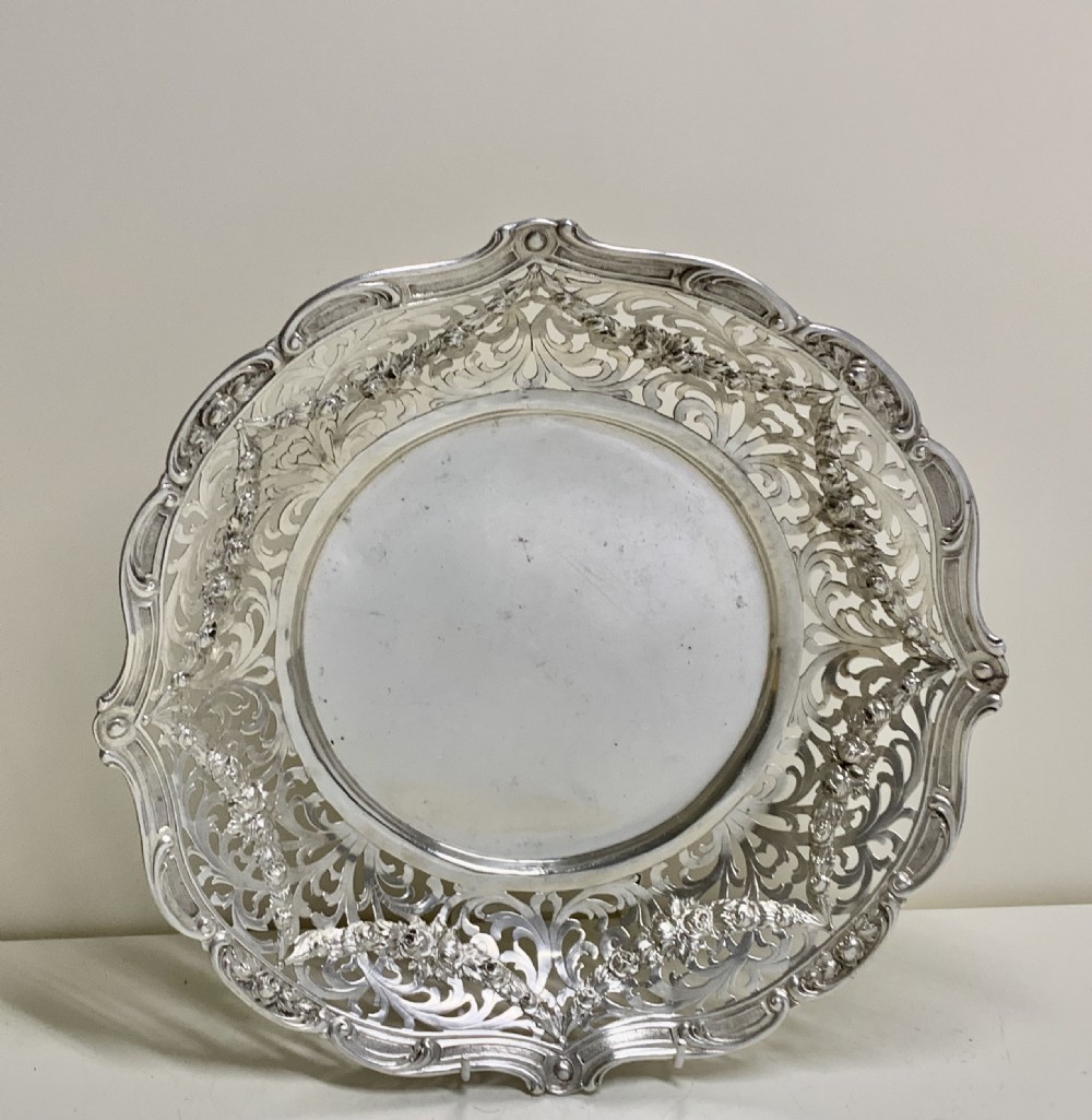 A circular antique solid silver bread basket featuring intricate hand-pierced fretwork, repousse floral swags, and a contoured scalloped rim. View III