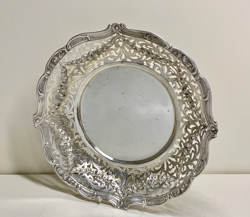 A circular antique solid silver bread basket featuring intricate hand-pierced fretwork, repousse floral swags, and a contoured scalloped rim. View V
