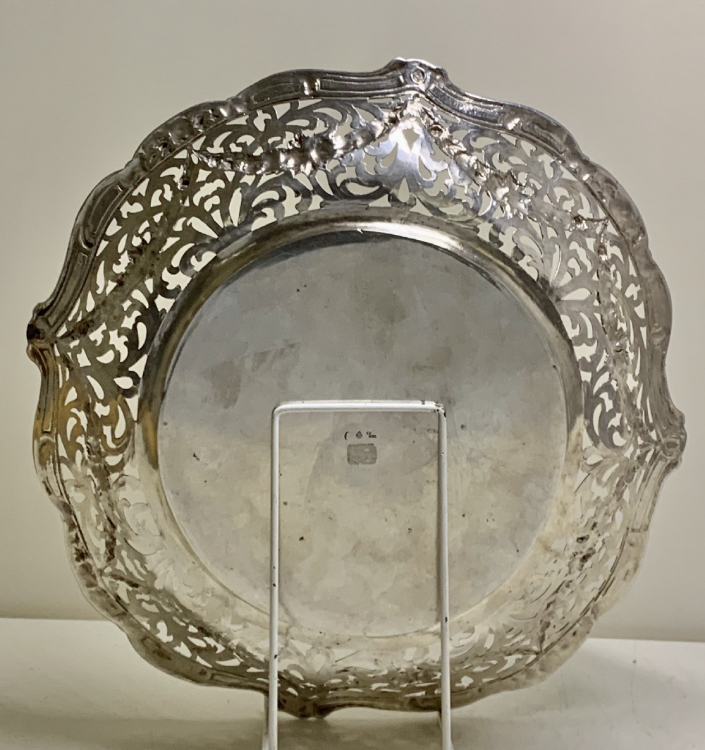 A circular antique solid silver bread basket featuring intricate hand-pierced fretwork, repousse floral swags, and a contoured scalloped rim. View VII