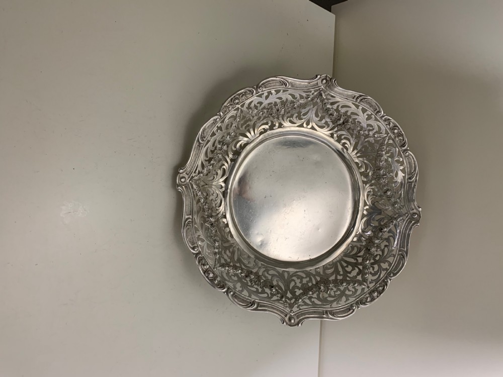 A circular antique solid silver bread basket featuring intricate hand-pierced fretwork, repousse floral swags, and a contoured scalloped rim. View X