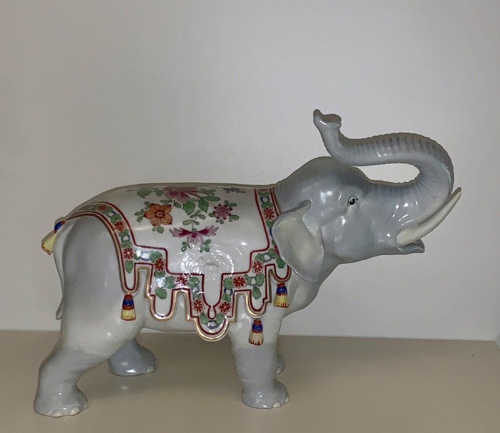 A large Dresden porcelain elephant figure painted in grey with a raised trunk and an ornate, colourful hand-painted saddle blanket. View II