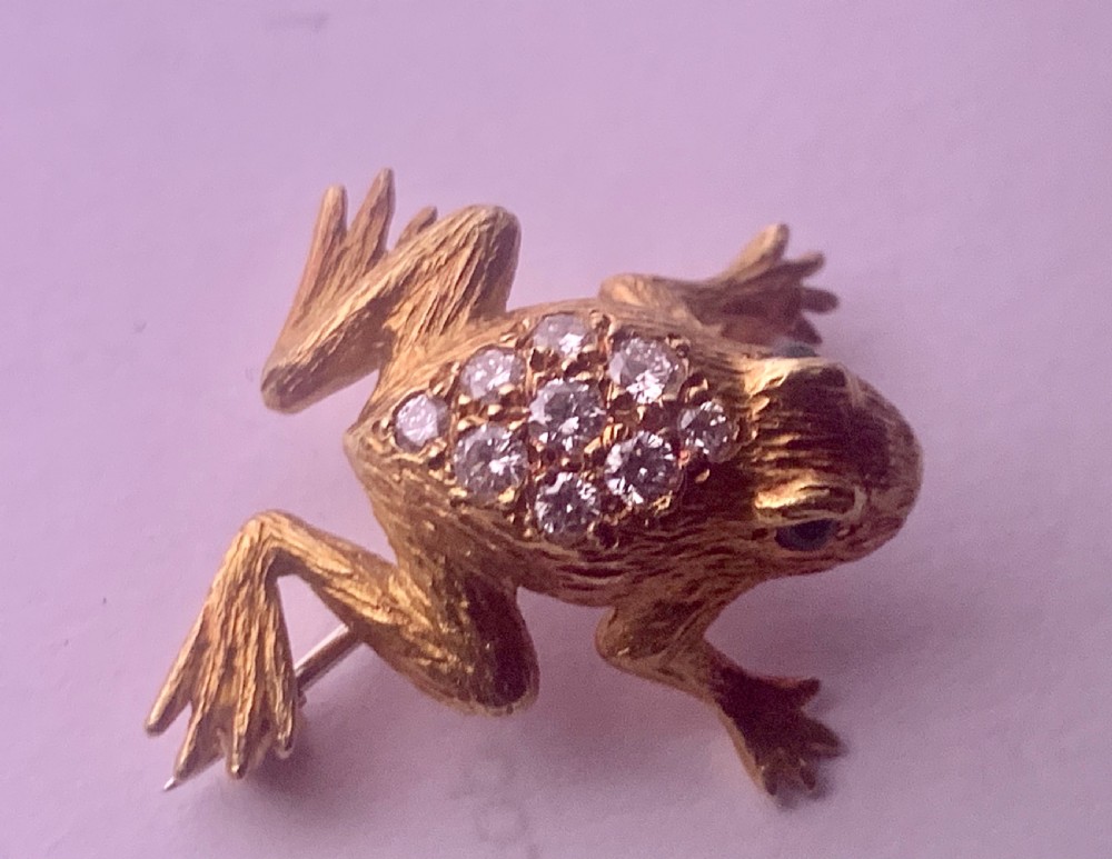 A textured gold frog brooch set with diamonds along its back and green gemstone eyes. View VI