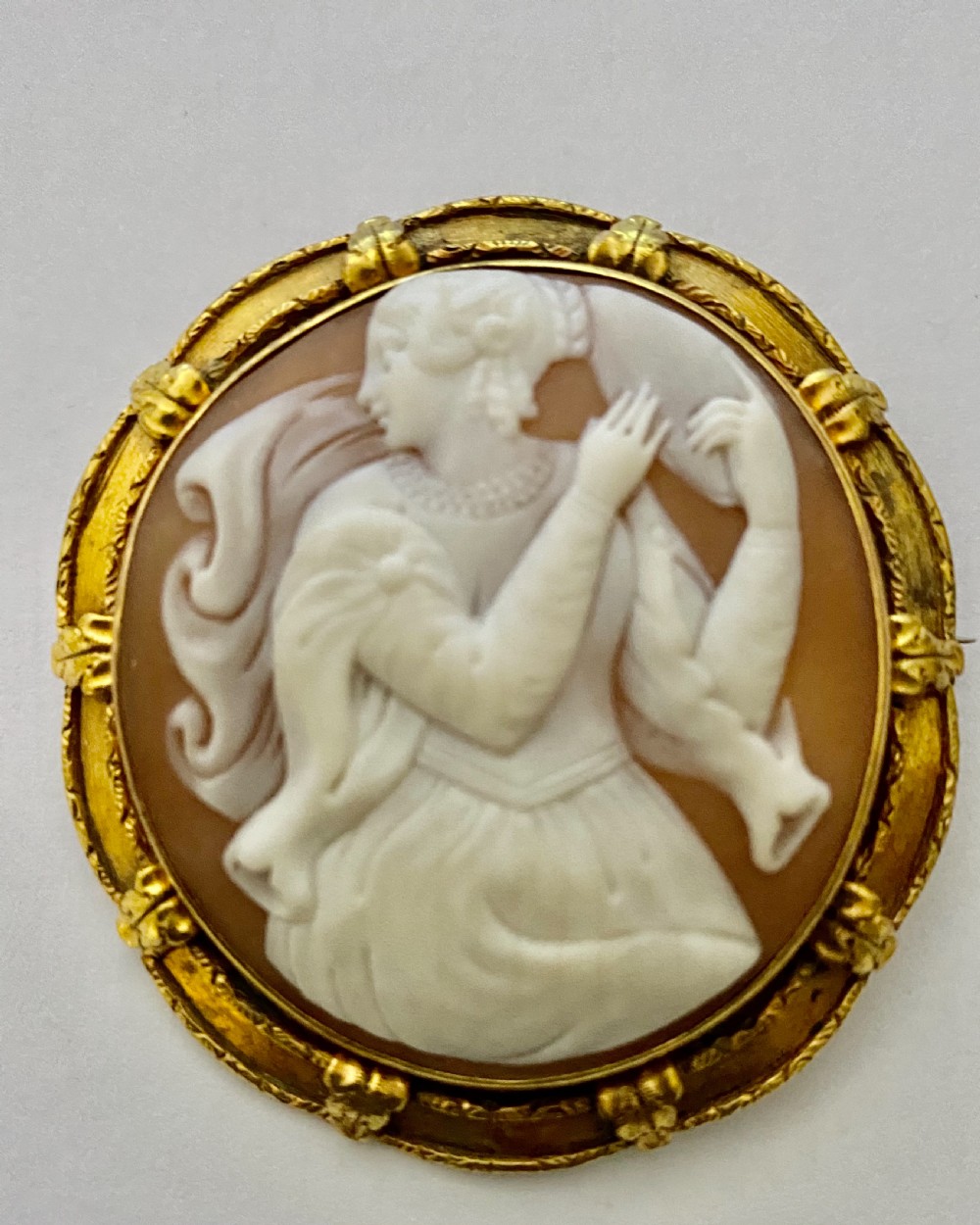 An antique circular brooch featuring a hand-carved shell cameo of a classical female figure set in a textured 15ct yellow gold frame. View II