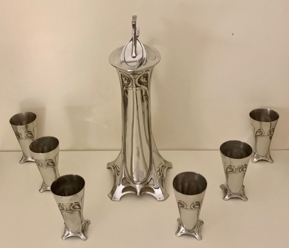 An Art Nouveau silvered pewter liqueur set comprising a tall spouted decanter with organic handles and six matching small tapered cups. View III