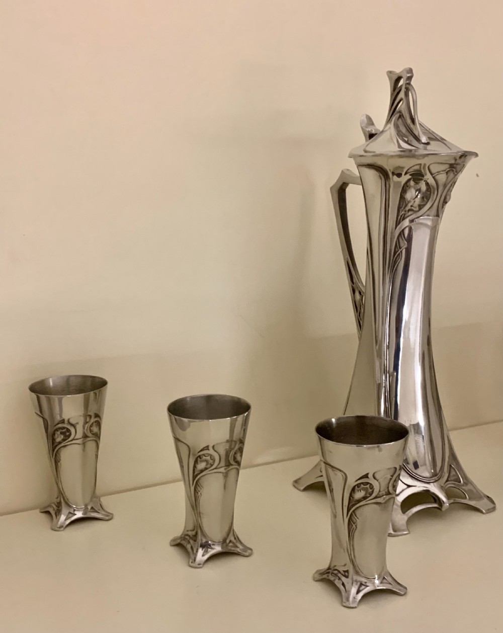 An Art Nouveau silvered pewter liqueur set comprising a tall spouted decanter with organic handles and six matching small tapered cups. View V