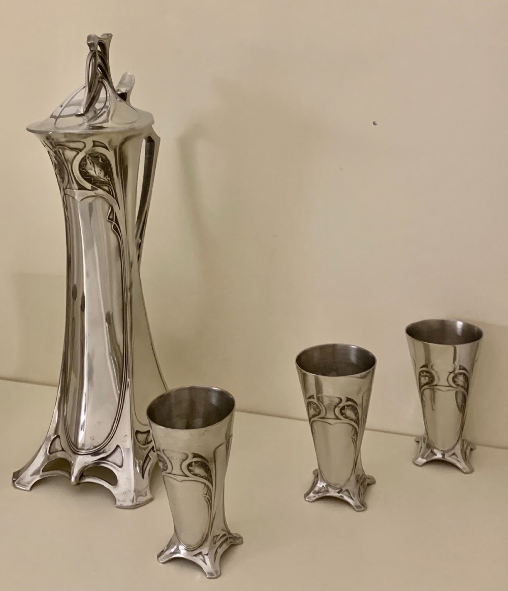 An Art Nouveau silvered pewter liqueur set comprising a tall spouted decanter with organic handles and six matching small tapered cups. View VI