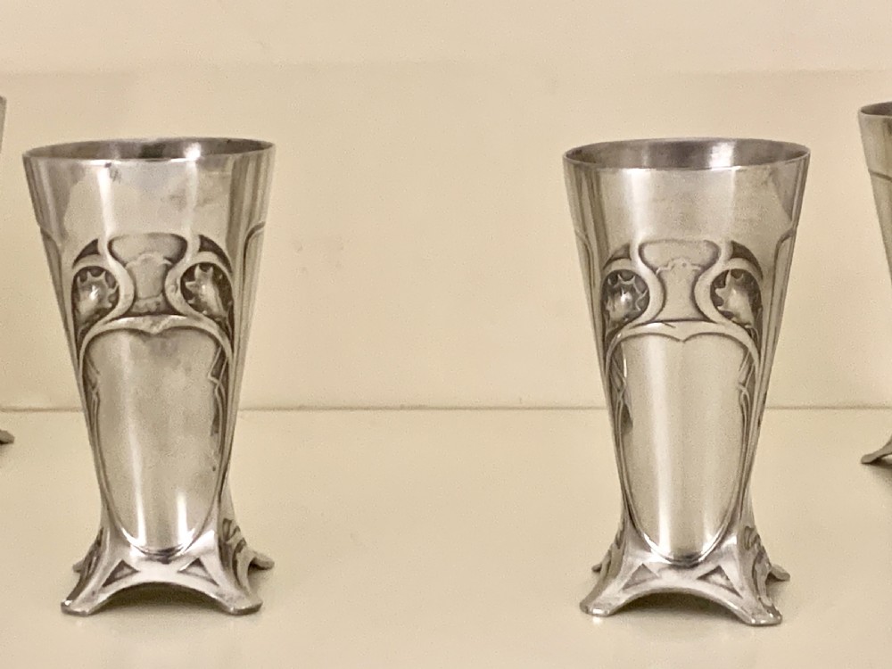An Art Nouveau silvered pewter liqueur set comprising a tall spouted decanter with organic handles and six matching small tapered cups. View VIII