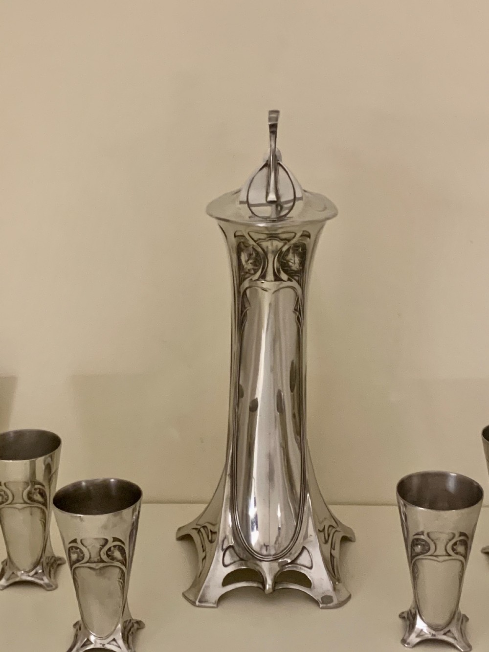 An Art Nouveau silvered pewter liqueur set comprising a tall spouted decanter with organic handles and six matching small tapered cups. View XXIII