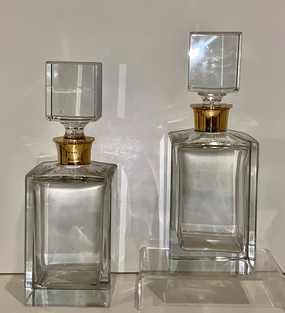 A pair of rectangular clear glass spirit decanters featuring gold-toned silver collars around the necks and matching square glass stoppers. View VIII