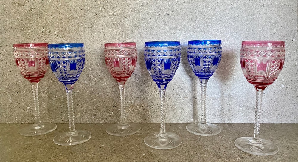 A set of six cut-to-clear crystal wine glasses with alternating cobalt blue and ruby red bowls on tall faceted stems.