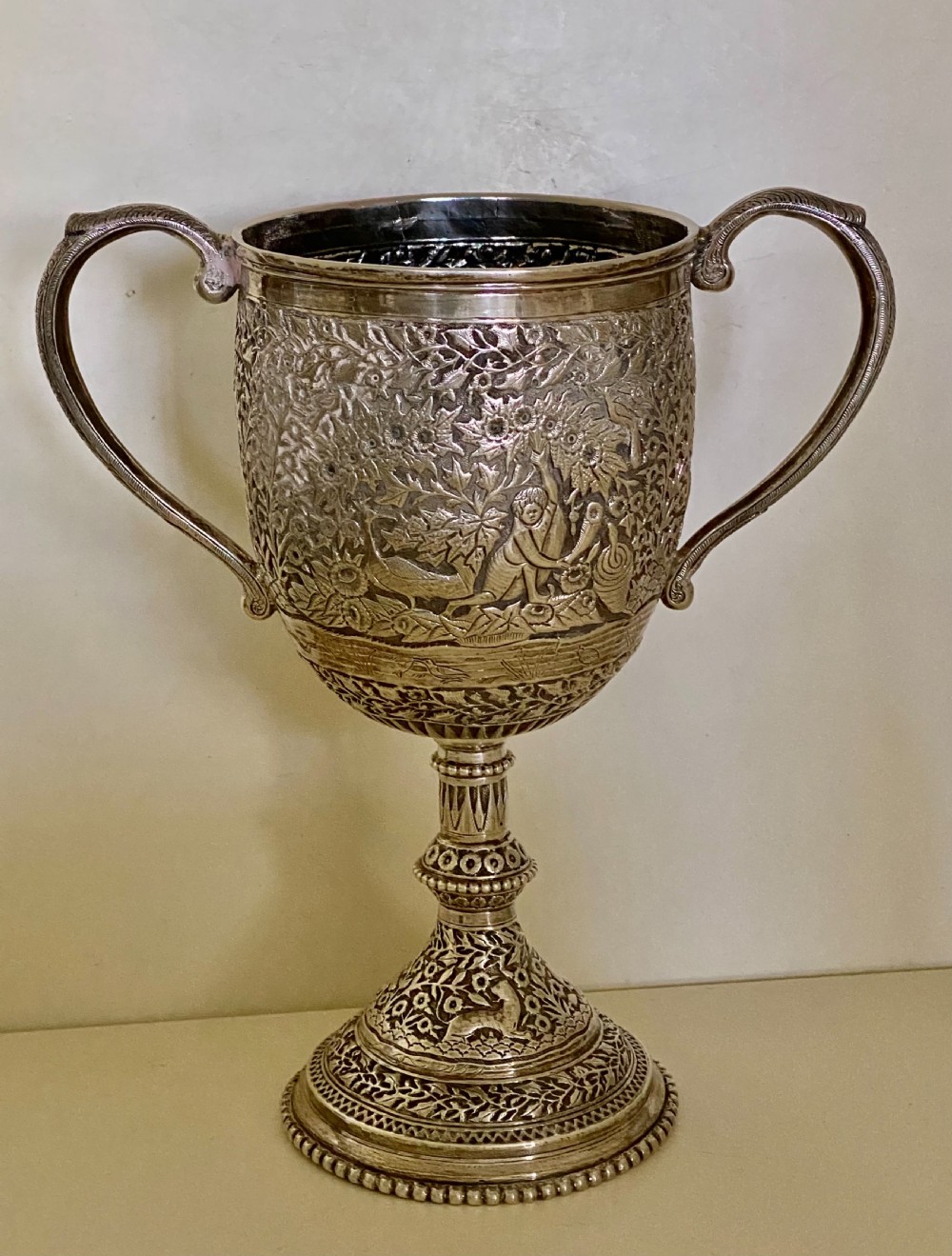 A 19th-century Indian Kutch silver trophy cup featuring dense chased floral motifs, twin scrolled handles, and an engraved central cartouche. View VI